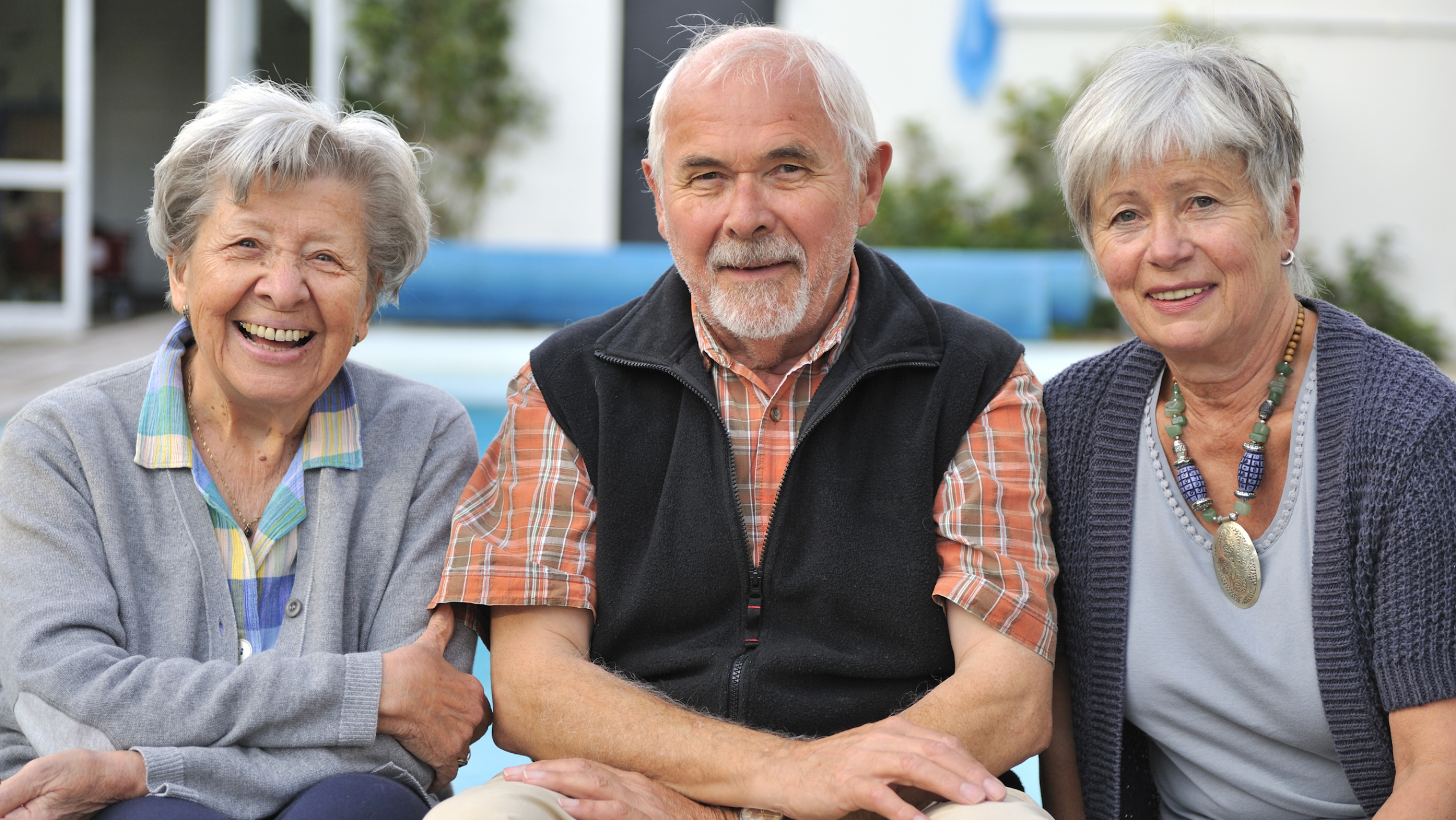 zwei Seniorinnen und ein Senior blicken in die Kamera und lächeln