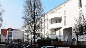 Hellgraue Gebäudezeile mit 4 Etagen, Balkone, im Winter. Vorne Parkplätze mit Fahrzeugen. Hellgraue Gebäudezeile mit 4 Etagen, Balkone, im Winter. Vorne Parkplätze mit Fahrzeugen.