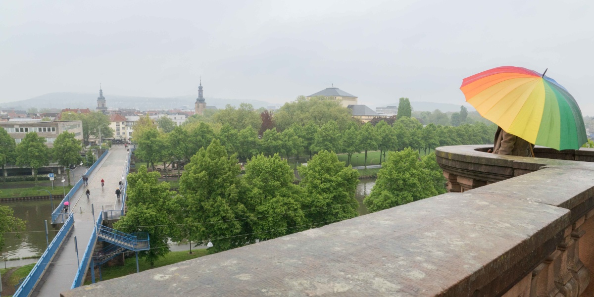 Eine Person mir regenbogenfarbenen Regenschirm steht auf de Saarbrücker Schlossmauer.