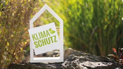 Weißes Haus mit der Aufschrift "Klimaschutz" in einer Waldidylle