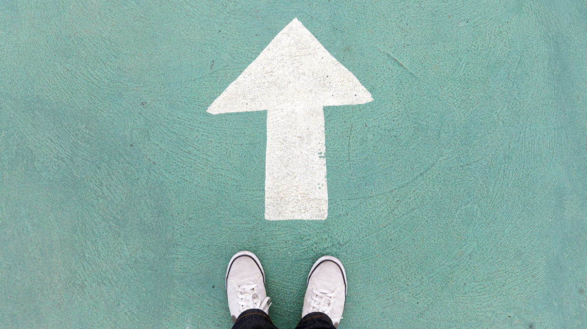 Auf dem Betonboden stehende Schuhe und weißer Wegweiser, um weiter zu gehen