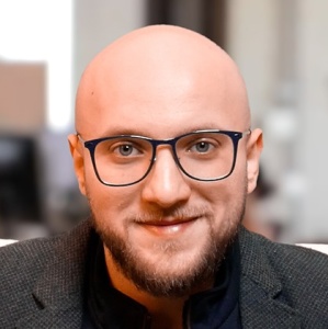 Portrait / Frontalaufnahme des Geschäftsführers Anas Alakkad mit Brille und Businessdress, lächelnd