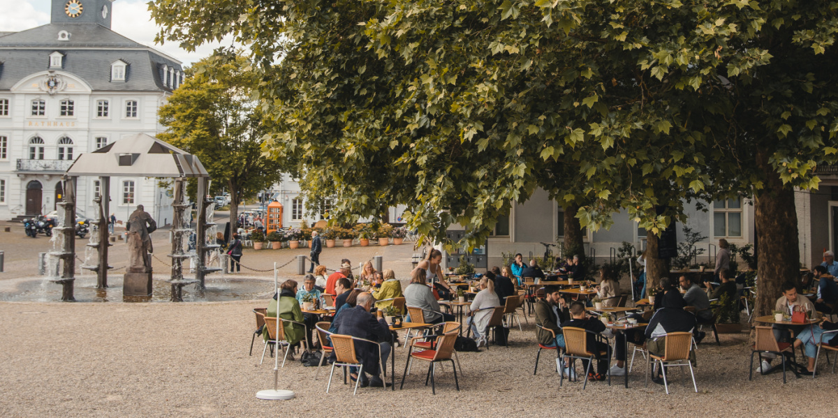 Außenansicht Café am Schloss: Tische unter großen Baum mit Blick auf das Alte Rathaus Saarbrücken