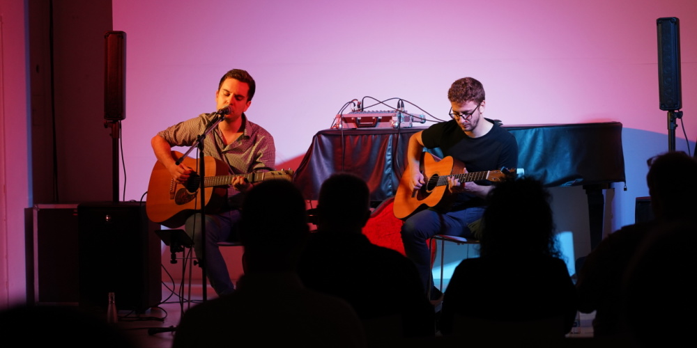 Veranstaltungsraum der Stadtgalerie, Umrisse von einem Publikum, zwei männliche Gitarrenspieler auf der Bühne