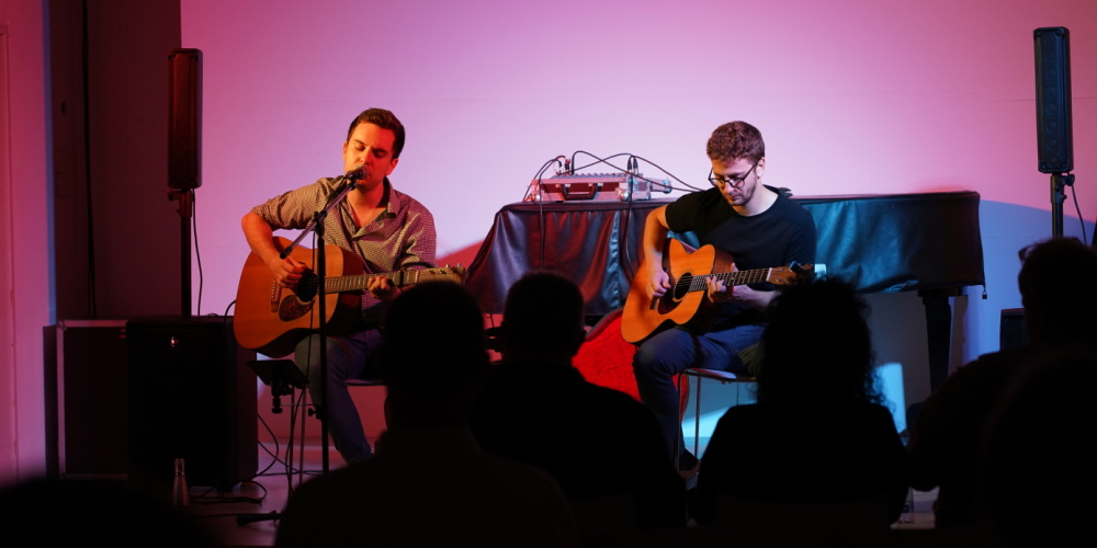 Veranstaltungsraum der Stadtgalerie, Umrisse von einem Publikum, zwei männliche Gitarrenspieler auf der Bühne