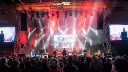 Eine rot beleuchtete Bühne mit Band und großem Publikum