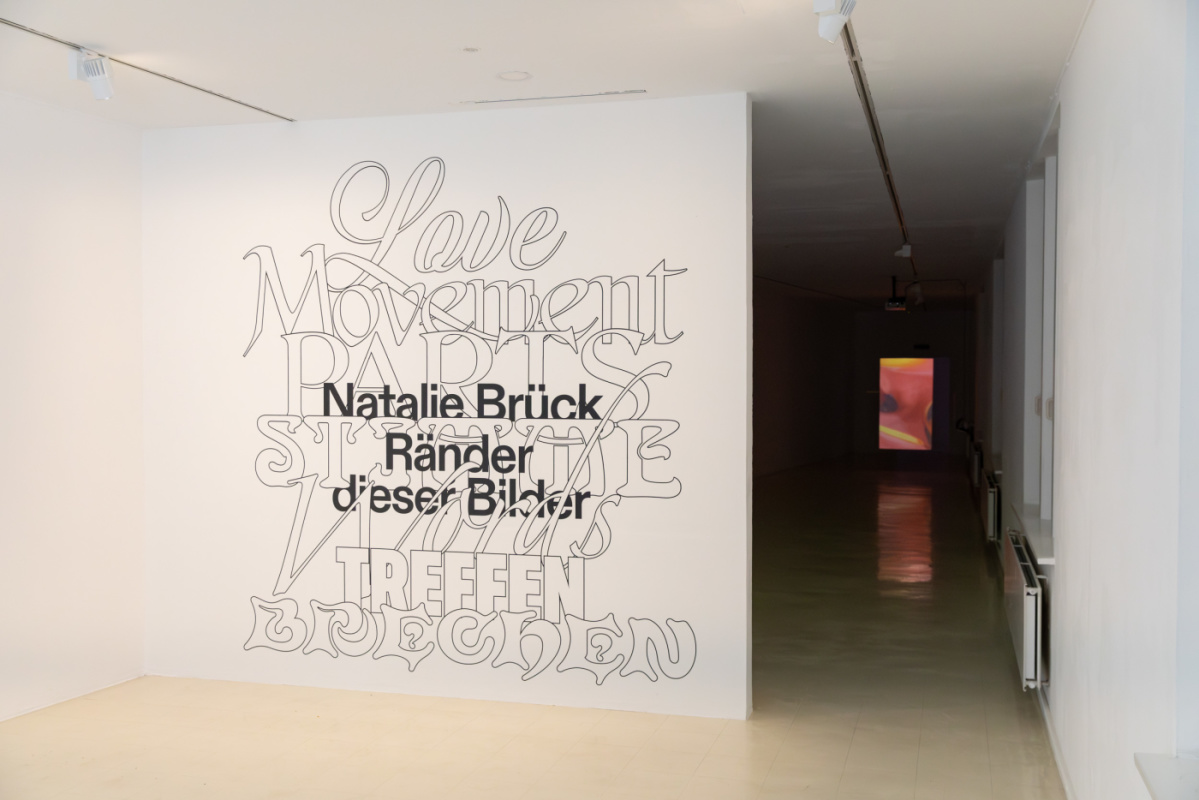 Schrift auf Wand, im Hintergrund eine Videoprojektion