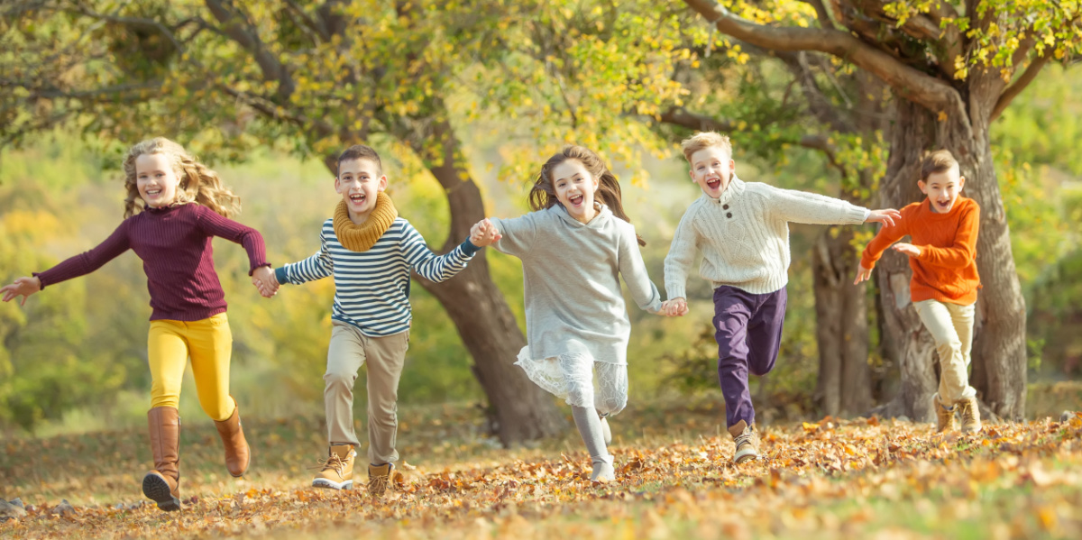 Fünf Kinder rennen über eine herbstliche Wiese, Im Hintergrund Bäume mit buntem Laub