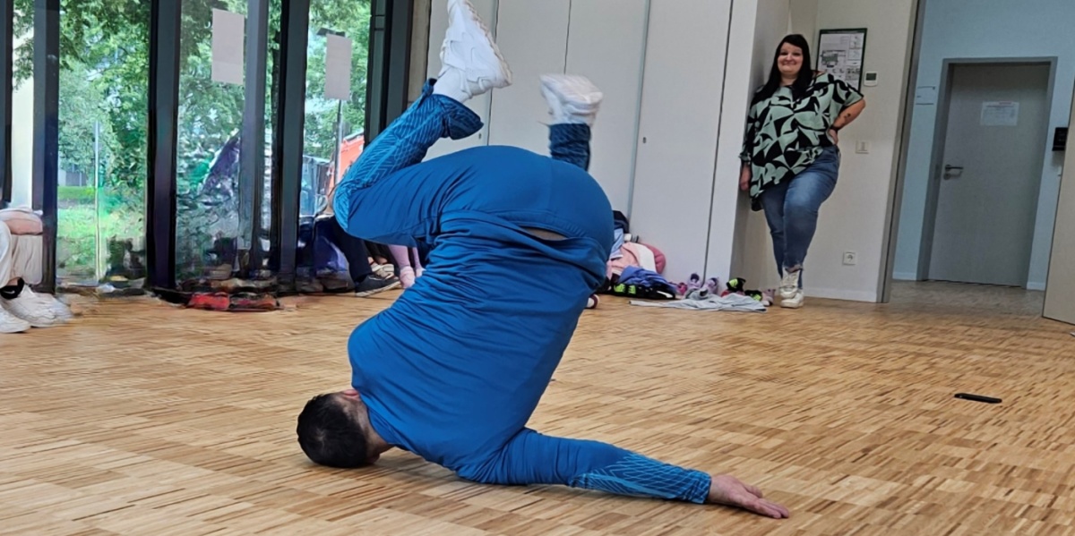 Breakdancer Gengis Ademoski in blauem Trainingsanzug macht eine Breakdance Bewegung