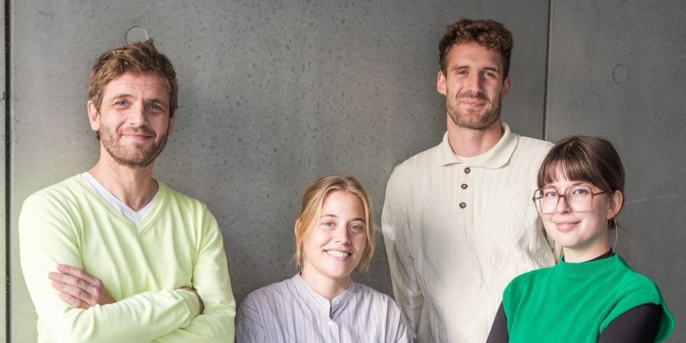 Porträt einer Gruppe von 4 Personen, die vor einer grauen Wand steht 