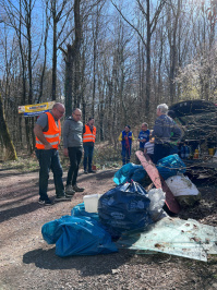 Picobello 2025: Müll im Vordergrund, im Hintergrund zwei Menschen mit Warnwesten im Wald