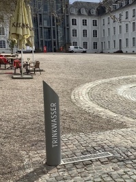 Trinkwasserbrunnen aus Edelstahl im Vordergrund, im Hintergrund das Saarbrücker Schloss