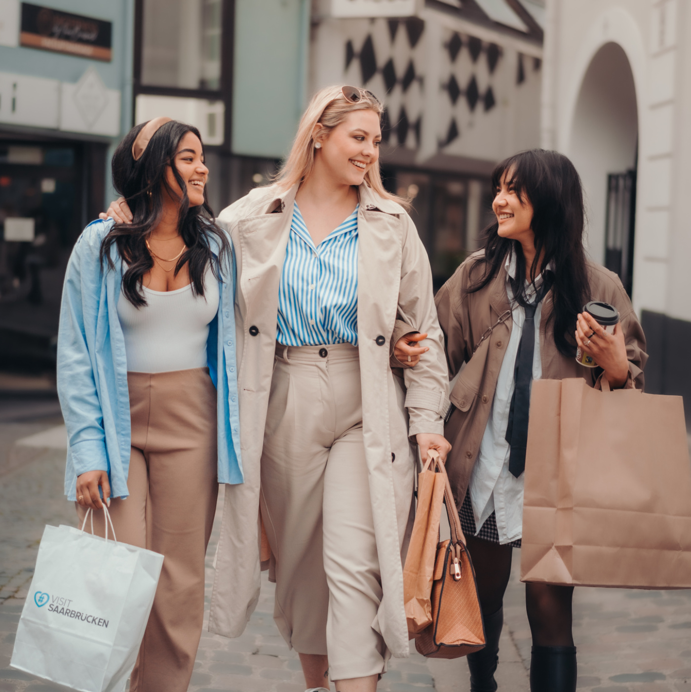 Drei lächelnde Freundinnen mit Shoppingtüten in der Saarbrücker Innenstadt