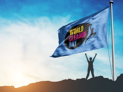 Rechts im Bild eine Flagge mit der Aufschrift World Cleanup Day, darunter die Silhouette eines Menschen, im Hintergrund Sonnenuntergang