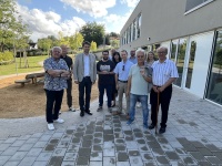 Eine Gruppe Menschen posiert neben auf einem gepflasterten Hof vor einem Haus neben einer Grünfläche 
