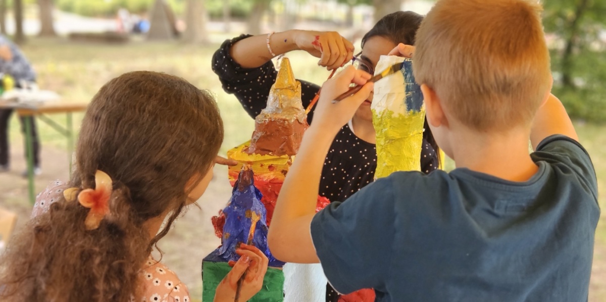 drei Kinder basteln draußen einen bunten Turm