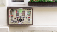 Kaugummiautomat vor einer weißen Hauswand mit Blumenkasten