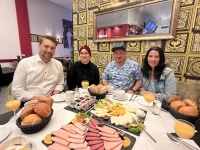 Vier Personen sitzen um einen reich gedeckten Tisch mit Brötchen und diversen Aufschnitten