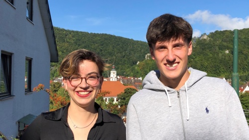 Eine junge Frau mit Brille und kurzen Haaren sowie ein junger Mann lächeln in die Kamera