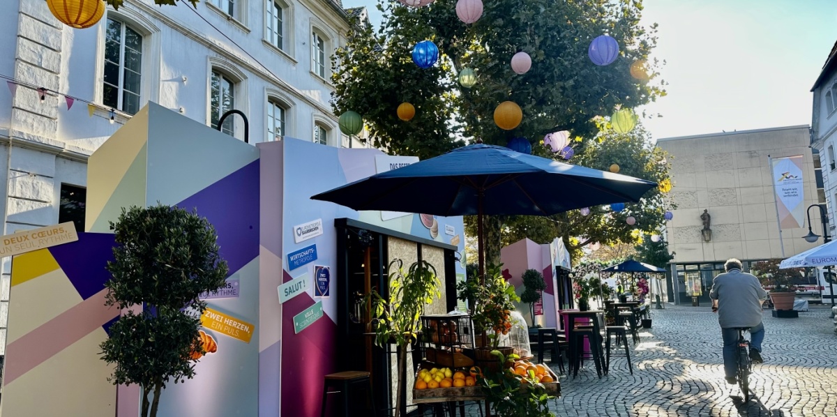 Stehtische, Sonnenschirme, bunte Stände und Lampions im Bäumen