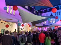 Eine Band spielt in einem Innenhof, davor Publikum und darüber sind Lampions angebracht