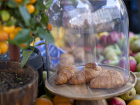 Zwei Croissants unter Glasglocke auf Marktstand, dahinter Früchte