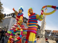 Bunt gekleidete Stelzenläufer halten bunte Ringe hoch