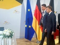 OB Uwe Conradt und der französische Präsident Emmanuel Macron gehen gemeinsam auf einen Tisch zu, dahinter Flaggen