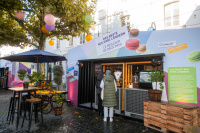 Ein Verkaufsstand mit der Aufschrift „Das Beste aus zwei Ländern“, davor eine Person in grüner Weste, über dem Stand bunte Laternen.