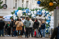 Blumenbogen aus weißen und blauen Blüten, darunter gehen und stehen mehrere Personen.
