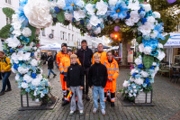 Stadtreiniger in orange farbenen Arbeitskleidern ein Mann in dunkler Kleidung und zwei Kinder unter einem herzförmigen Bogen dekoriert mit Blumen