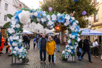 Zwei Personen posieren unter einem mit weißen und blauen Blumen dekorierten Herzbogen