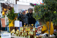 Zwei Personen schauen auf einen Marktstand mit Honiggläsern und Bienenprodukten, im Vordergrund Pflanzen.