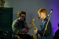 Zwei Musiker mit Saxophonen stehen nebeneinander, einer spielt, der andere hält sein Instrument, im Vordergrund ein Mikrofon.