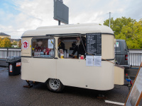 Retro-Foodtruck verkauft Kaffee und heiße Schokolade, Besucher bestellen am weißen Verkaufswagen mit Preistafel.
