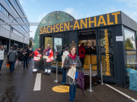 Informationspavillon des Landes Sachsen-Anhalt mit gelber Aufschrift und Besuchern vor Ort in Saarbrücken.