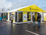 Gelbes Ausstellungszelt des Landes Baden-Württemberg mit der Aufschrift „The Länd“, Besucher informieren sich über Angebote.