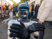 Roboter mit leuchtendem Gesichtsschild präsentiert sich den Besuchern, Kinder und Erwachsene schauen zu.