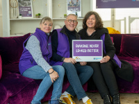 Drei Mitarbeitende der Diakonie Saar sitzen auf einem lila Sofa und halten ein Schild mit der Aufschrift „Diakonie never looked better“.