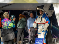 Frau probiert einen Raumanzug im Pavillon des Bundesministeriums für Forschung und Raumfahrt, Besucher fotografieren die Szene.