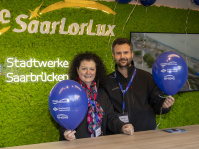 Modell einer Rakete „Space Buzz“ vor einem modernen Bürogebäude mit Zuschauern und Fahnen.