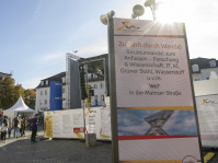 Großes Plakat mit der Aufschrift „Zukunft durch Wandel“ vor einer Bühne in der Innenstadt mit Besuchern.