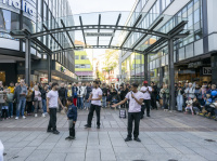 Straßenszene in der Rotenhofstraße mit Straßenkünstlern, Kind in der Mitte und großem Publikum vor Geschäften.