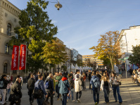Menschen flanieren durch eine Straße mit Bäumen, alten Gebäuden und roten Fahnen mit Aufschrift „NDR Nord“.
