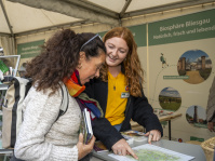 Infostand der Biosphäre Bliesgau, Mitarbeiterin zeigt einer Besucherin einen Lageplan, Flyer liegen auf dem Tisch.