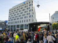 Große Menschenmenge vor einer Bühne mit Bildschirm „Reisen für Alle“ auf einem Platz neben dem H2 Hotel.