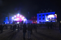 Abendveranstaltung mit beleuchteter Bühne, großem Bildschirm und Zuschauermenge im Freien.