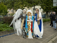 Drei Personen in aufwendigen Fantasy-Kostümen mit Flügeln und langen Gewändern posieren für ein Foto.