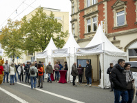 Informationsstände in weißen Zelten auf einer Straße in Saarbrücken, Menschen stehen im Gespräch davor.