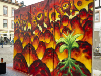 Fertiges Graffiti-Wandbild mit leuchtenden Augenmotiven in Rot- und Gelbtönen sowie einer grünen Pflanze im Vordergrund.